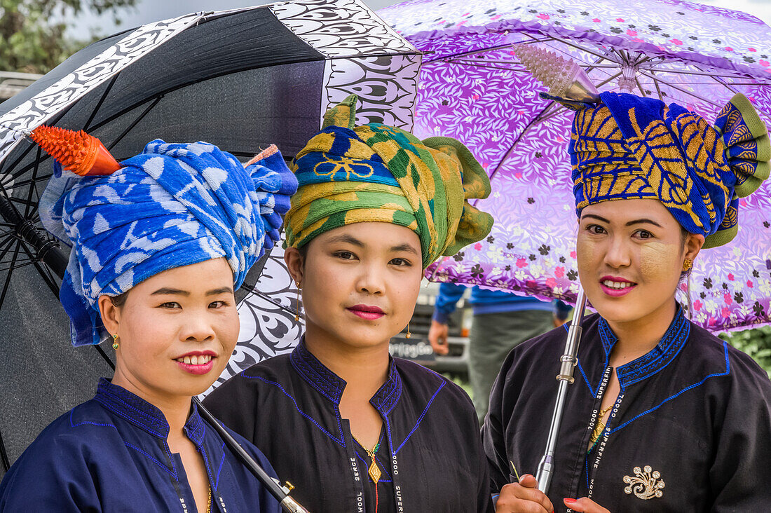 Frauen des Pa'O-Stammes tragen bunte Kopfbedeckungen und stehen mit Regenschirmen; Yawngshwe, Shan-Staat, Myanmar