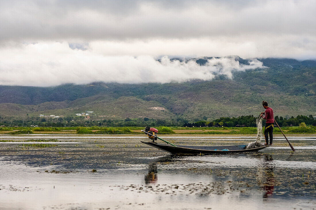 Ein Fischer steht mit Netz und Paddel am Rand des Bootes auf dem Inle-See; Yawngshwe, Shan-Staat, Myanmar