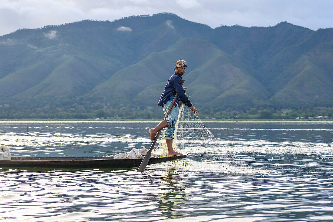 Traditional fishing standing on the tip of the boat with a net and paddle; Yawngshwe, Shan State, Myanmar