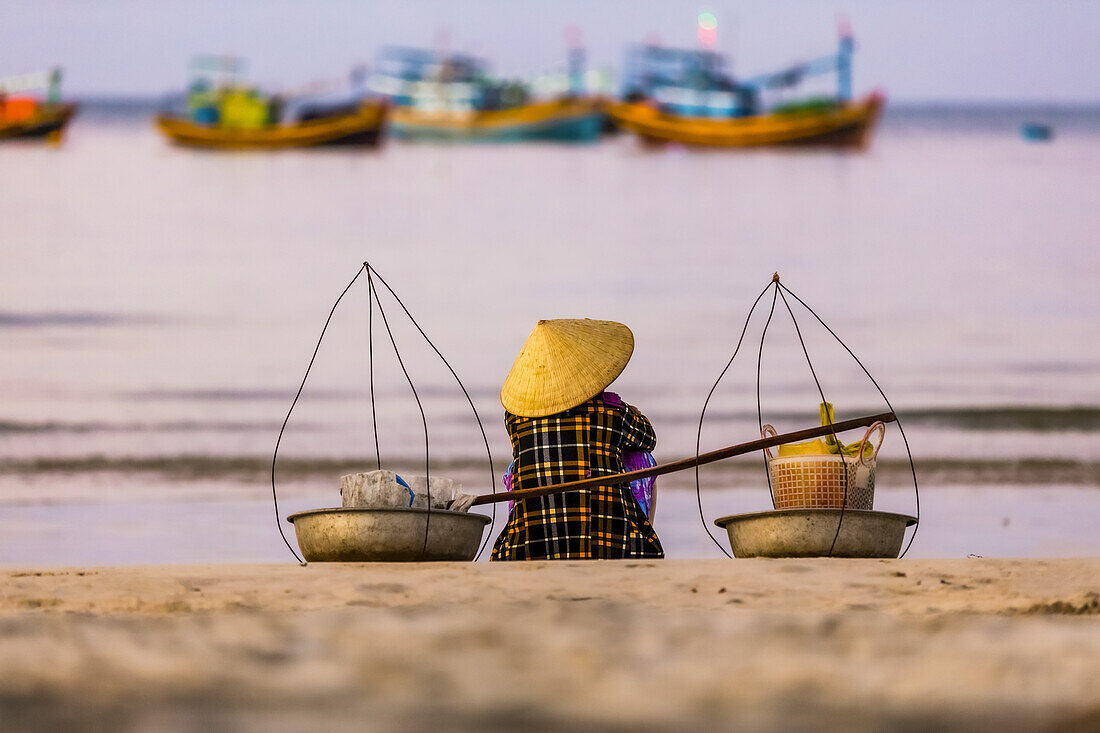 Eine Frau sitzt am Strand und schaut auf die zahlreichen Fischerboote im Wasser vor der Küste, Kap Ke Ga; Ke Ga Island, Vietnam