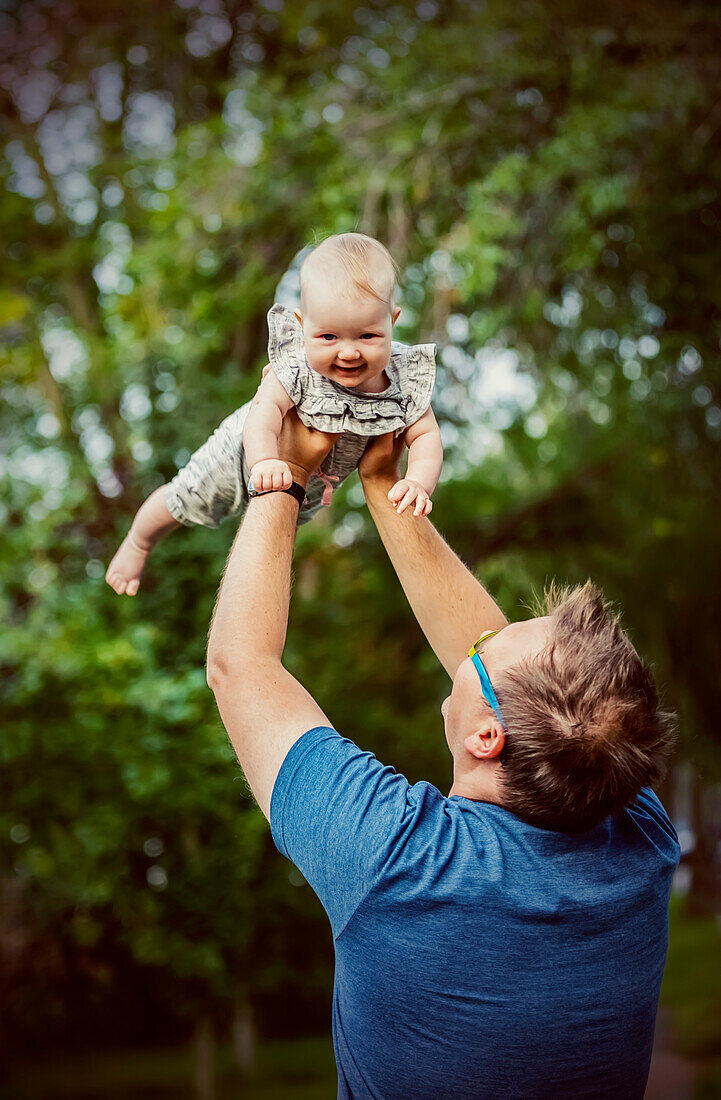 A father holding his baby girl in the air while outdoors during the fall; Edmonton, Alberta, Canada