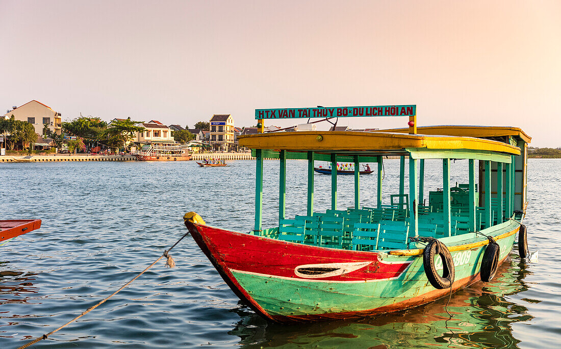 Colourful tour boat moored in the water along the waterfront at sunrise; Hoi An, Quang Nam Province, Vietnam