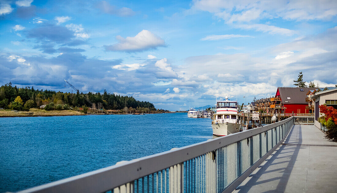 Boote im Hafen und Gehweg zu bunten Gebäuden am Hafen von La Conner, einer Stadt an der Küste des pazifischen Nordwestens; La Conner, Washington, Vereinigte Staaten von Amerika