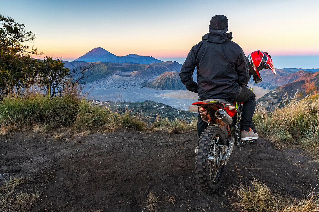 A man sitting on a motorcycle watches the sunrise at Bromo from a secret viewpoint, Bromo Tengger Semeru National Park; Pasuruan, East Java, Indonesia