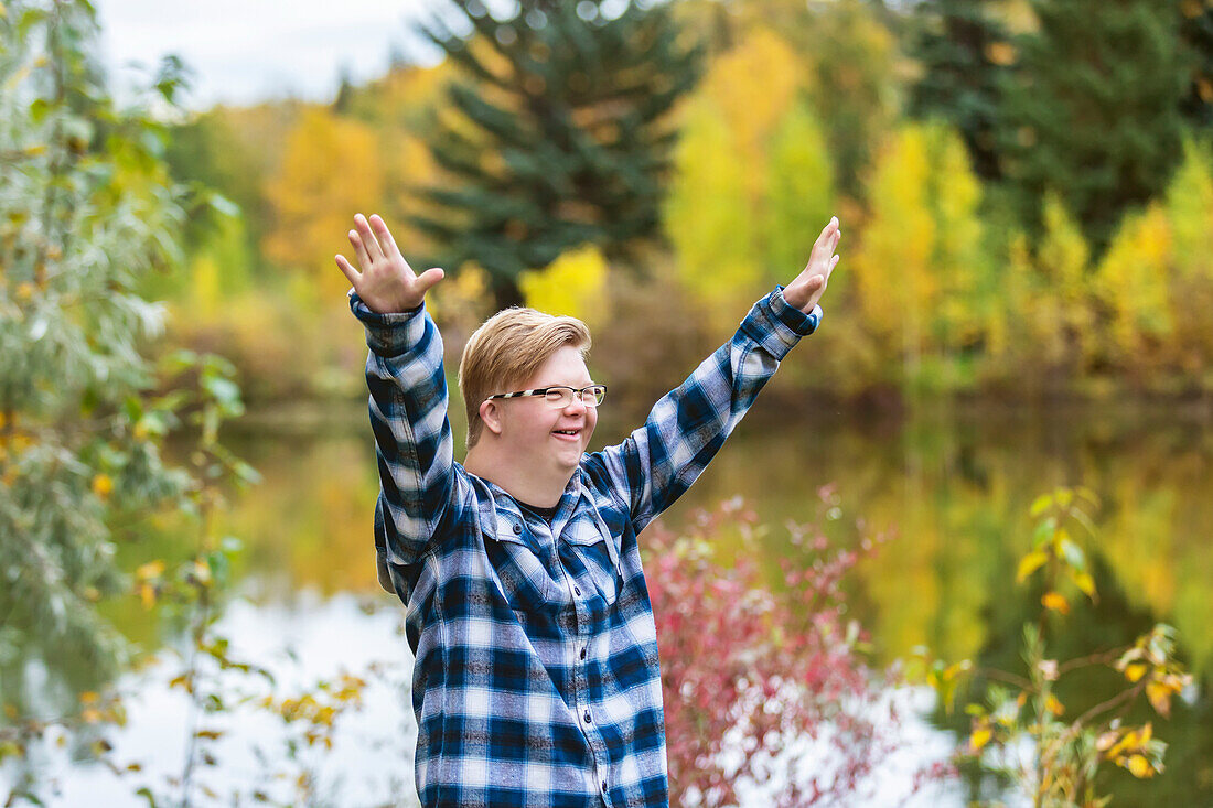 A young man with Down Syndrome raising his hands in worship to God, while in a city park on a warm fall evening: Edmonton, Alberta, Canada