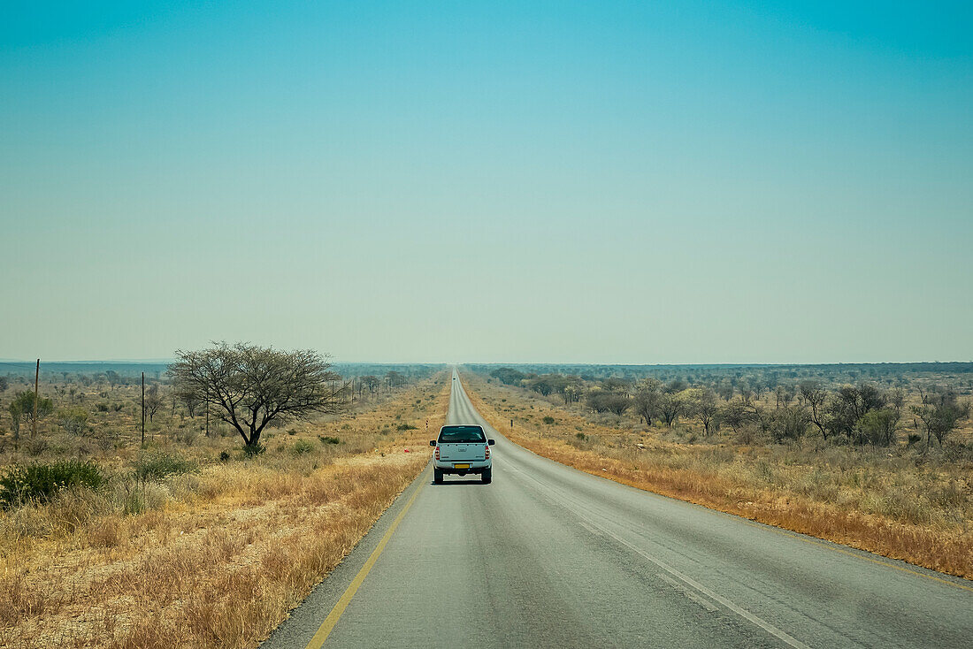 Ein Lastwagen fährt auf einer offenen Straße in der Wüste mit einem großen blauen Himmel am Horizont; Namibia