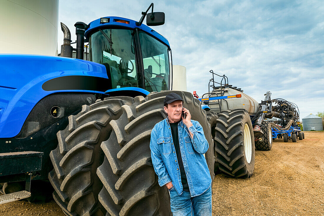 Landwirt benutzt ein Smartphone, während er auf einem Bauernhof neben den Geräten steht; Alberta, Kanada