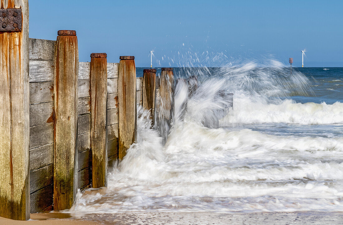 Wellen plätschern an der hölzernen Ufermauer und Windturbinen in der Ferne im Wasser an der Küste von Blyth; Blyth, Northumberland, England