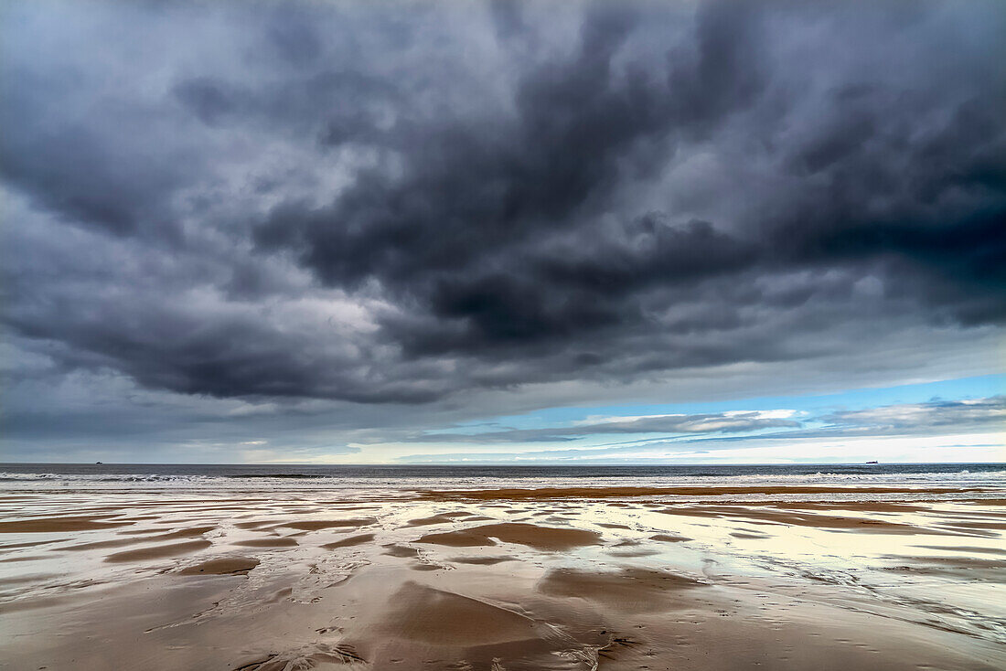 Dunkle Gewitterwolken über dem Atlantischen Ozean mit nassem Sandstrand im Vordergrund; South Shields, Tyne and Wear, England