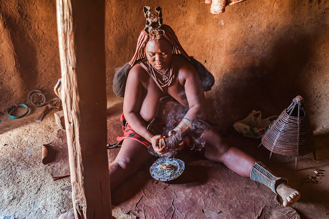 Himba woman preparing incense to wash her hair with the smoke, Himba village; Kamanjab, Namibia