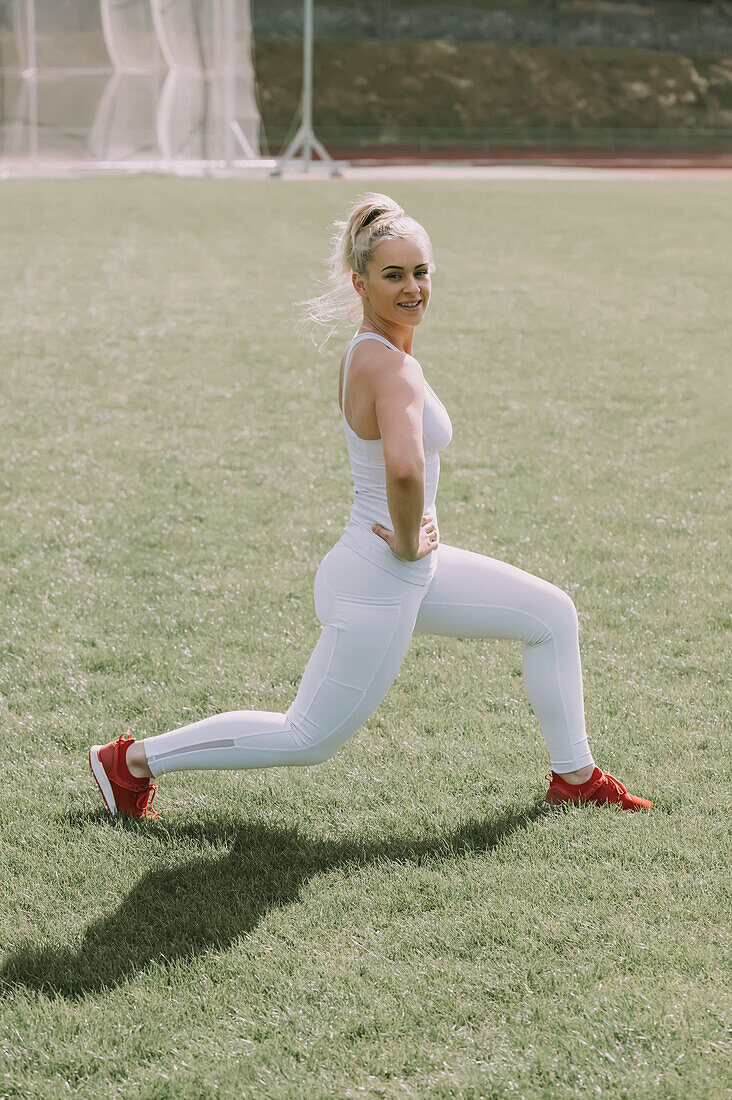 Woman stretching her leg muscles on a grass field; Wellington, New Zealand