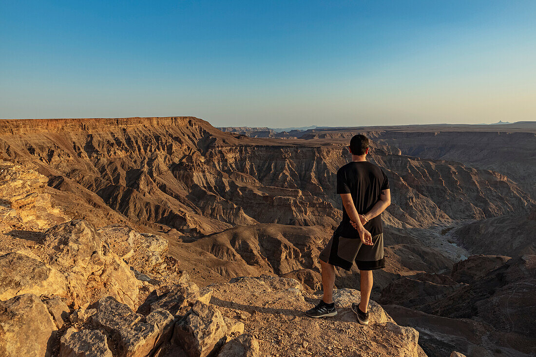 Männlicher Tourist steht auf einem Felsvorsprung mit Blick auf den Fish River Canyon; Namibia