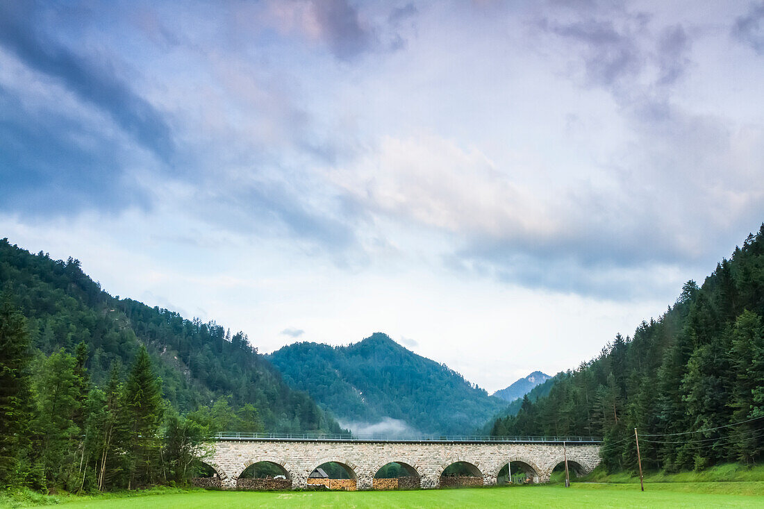 Old stone railway viaduct bridge crossing a grass field in a valley in the Austrian Alps; Wildalpen, Landl, Austria