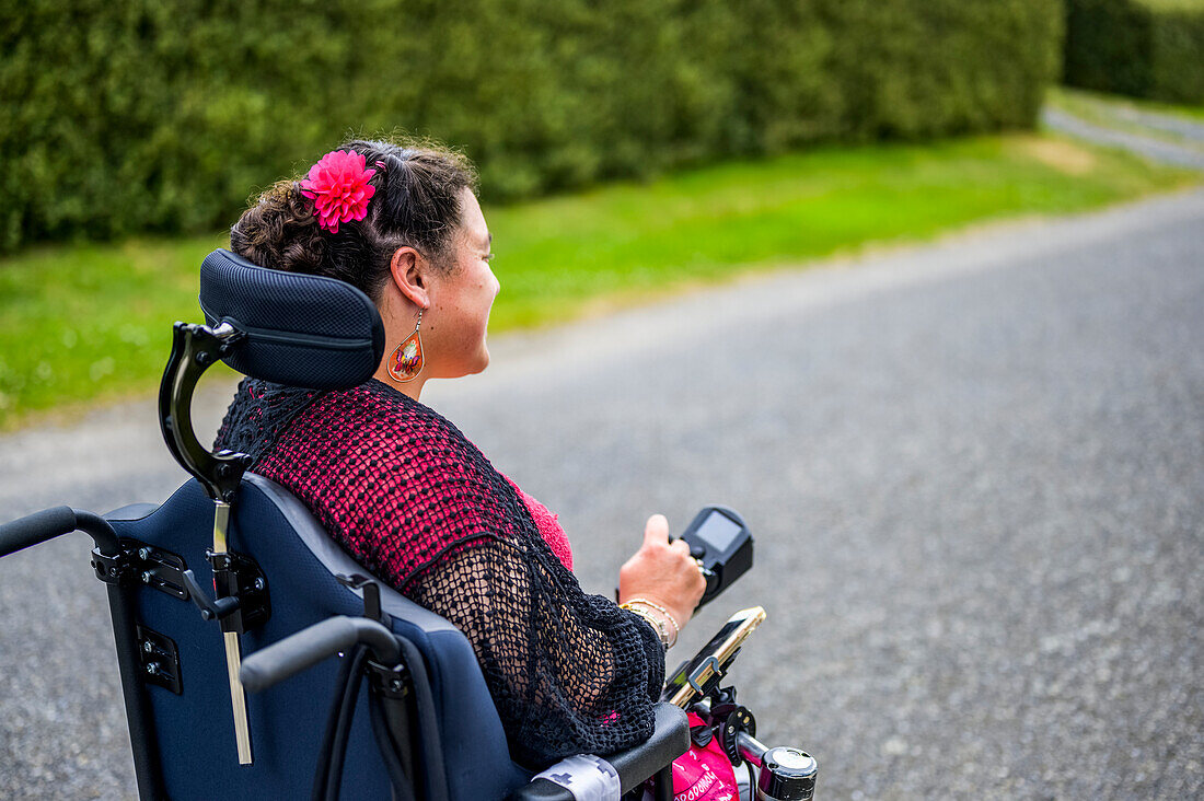 Maori-Frau mit Cerebralparese in einem Rollstuhl, die einen Bürgersteig entlangfährt; Wellington, Neuseeland