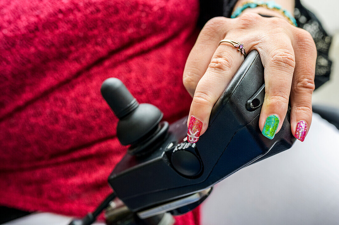 Maori-Frau mit Cerebralparese in einem elektrischen Rollstuhl mit Joystick und Reglern, Fingernägel mit Nagelmalerei; Wellington, Neuseeland
