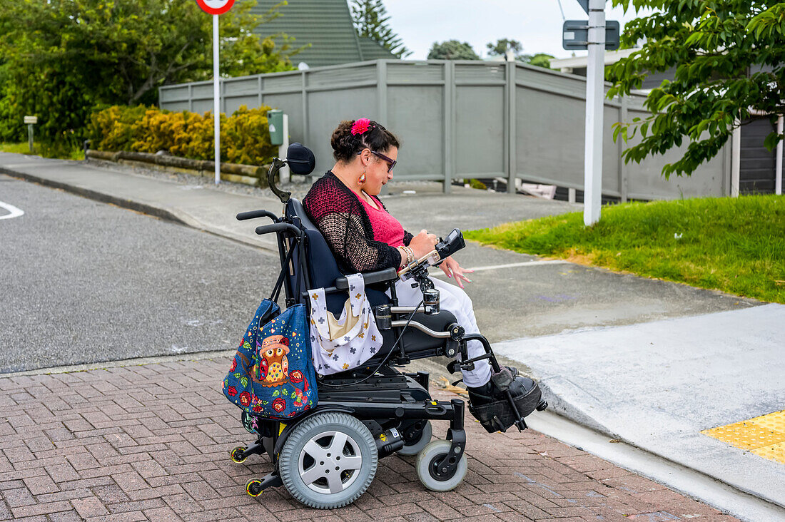 Maori-Frau mit Cerebralparese in einem Rollstuhl beim Überqueren einer Straße; Wellington, Neuseeland