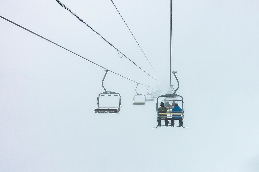 Downhill skiers ride on a chairlift through the clouds, Sun Peaks Resort; Sun Peaks, British Columbia, Canada