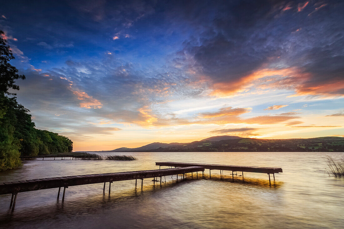 Dock am Ufer eines Sees mit Bergen im Hintergrund bei Sonnenaufgang; Two Mile Gate, County Clare, Irland