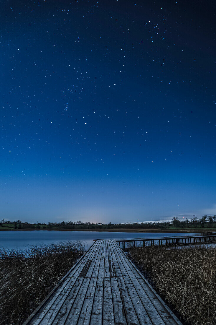 Holzsteg entlang des Lough Erne bei Nacht mit Sternen am Himmel; County Fermanagh, Irland