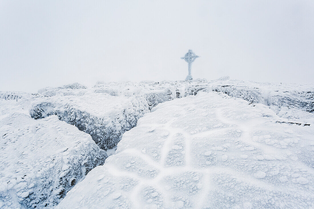 Gefrorene Eisformationen auf dem Gipfel des Berges Galtymor mit einem keltischen Kreuz im Winter, Galty Mountains; County Tipperary, Irland