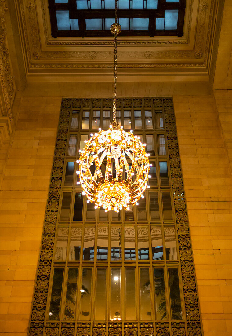 Beleuchteter und dekorativer runder Kronleuchter, der vor einem Spiegel in einem Gebäude in Manhattan hängt; New York City, New York, Vereinigte Staaten von Amerika