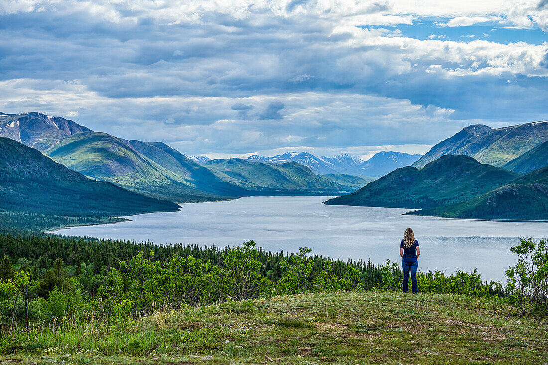Woman stands looking out at a lake and the vast Yukon Ranges; Whitehorse, Yukon, Canada