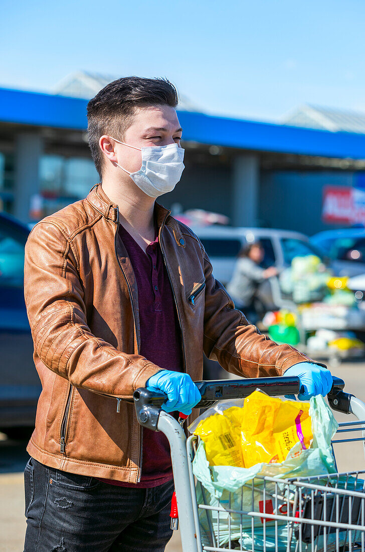 Ein junger Mann steht auf einem Parkplatz mit einem Einkaufswagen während der Covid-19-Weltpandemie; Edmonton, Alberta, Kanada