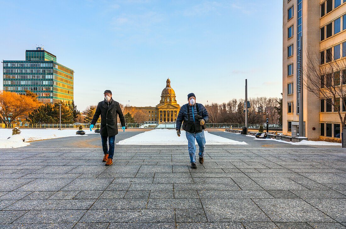 Ein Mann mit Maske und Handschuhen geht während der Covid-19-Weltpandemie auf einem Weg neben der Legislative spazieren; Edmonton, Alberta, Kanada