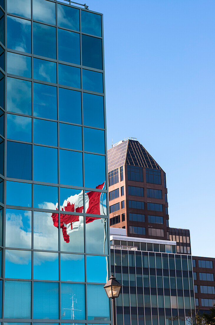 Nahaufnahme von Bürotürmen mit Himmel und kanadischer Flagge, die sich in den Fenstern spiegelt, Halifax, Nova Scotia, Kanada