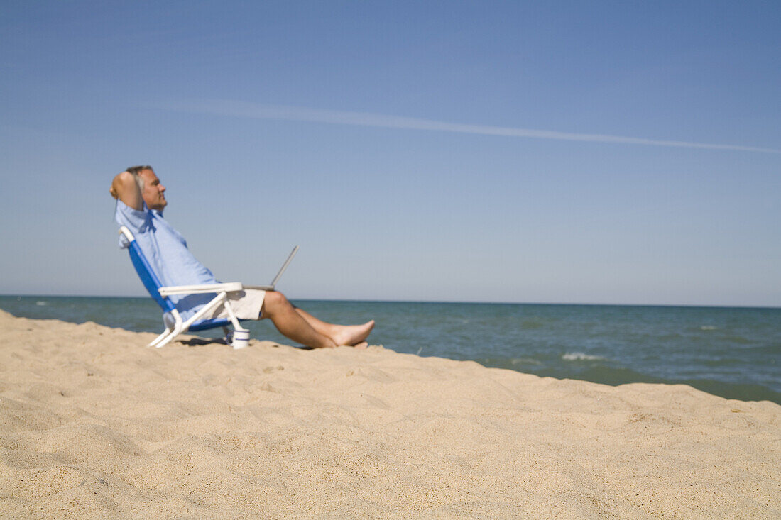 Mann sitzt am Strand und benutzt einen Laptop, Lake Michigan, USA