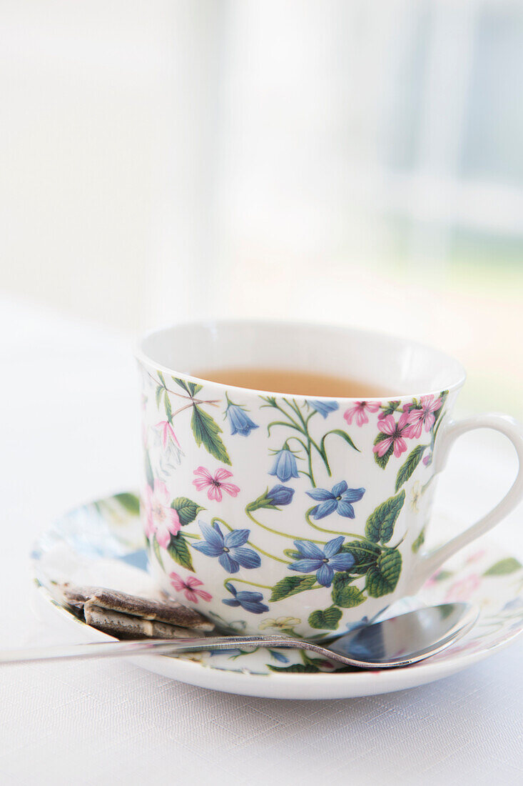 Tasse Tee in hübscher Blumentasse mit Untertasse und gebrauchtem Teebeutel, Studioaufnahme