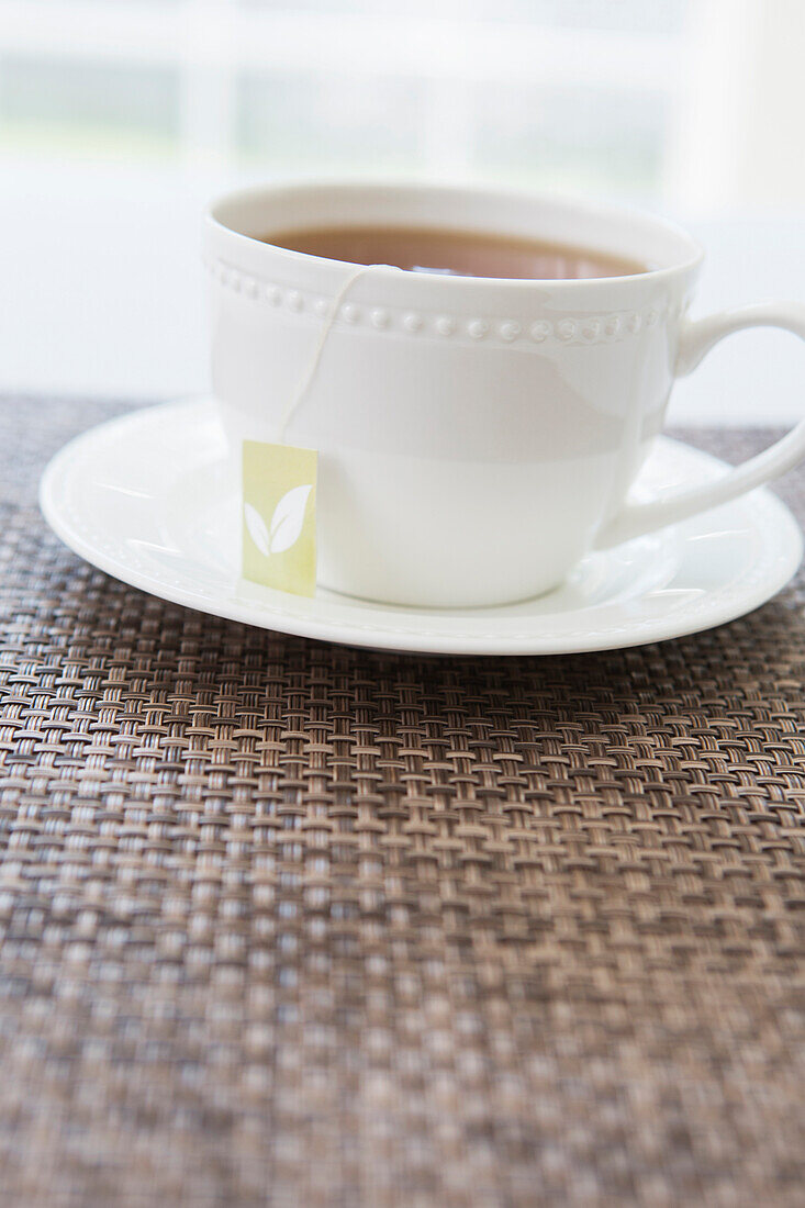 Cup of tea in white porcelain cup with saucer and tea bag, studio shot