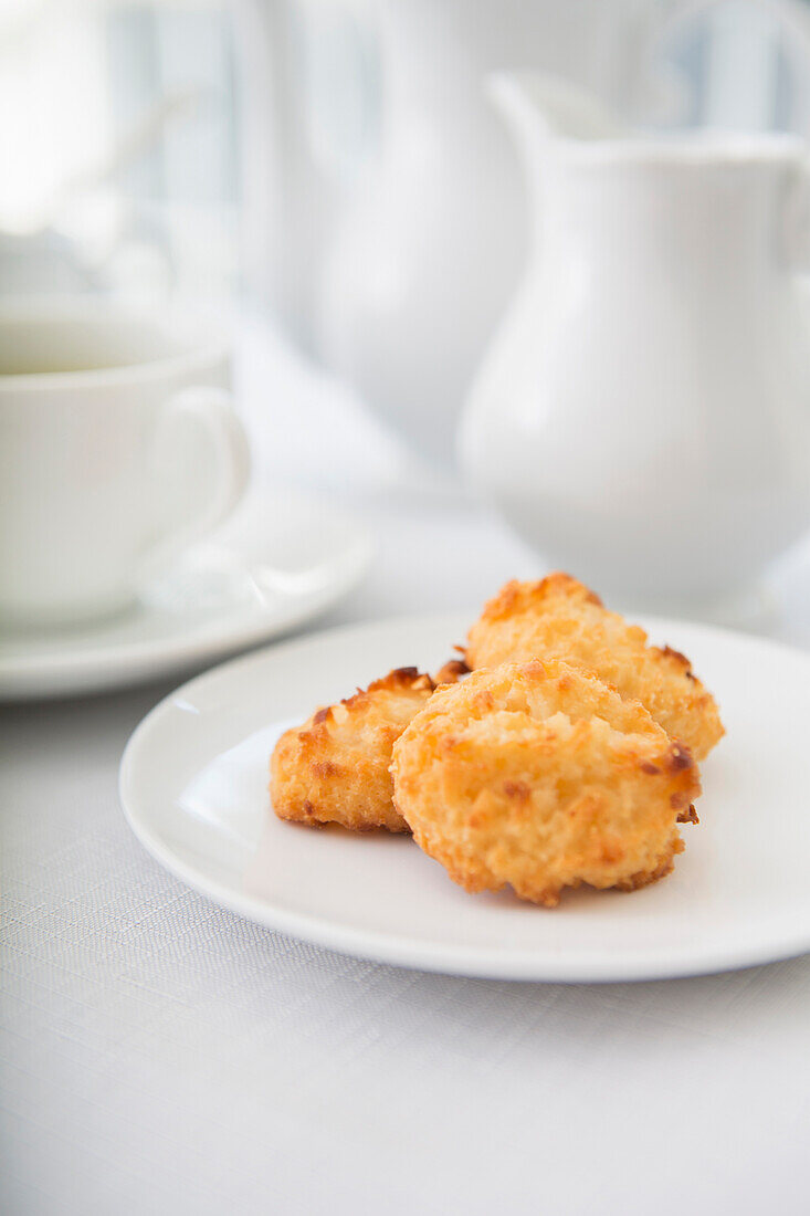 Plate of coconut macaroons, pastries with cup of tea and teaset, studio shot