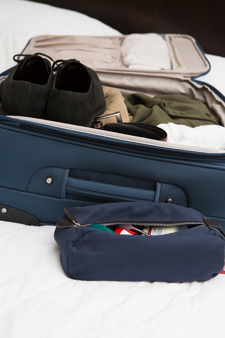 Männertoiletten-Reisetasche neben gepacktem Koffer auf dem Bett, USA