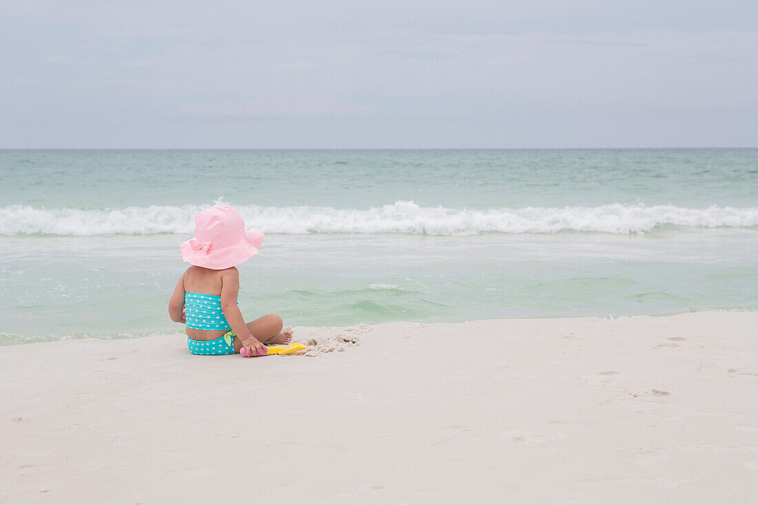 Rückenansicht eines kleinen Mädchens mit Sonnenhut am Strand und Blick auf den Ozean, Destin, Florida, USA