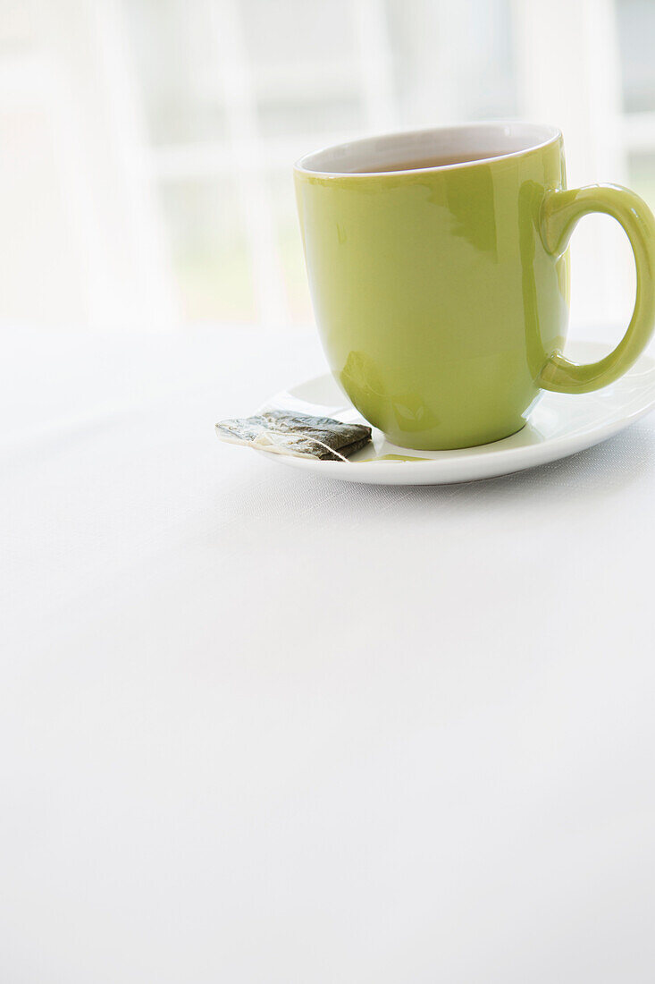 Gebrauchter Teebeutel auf Untertasse mit Tasse Tee in grüner Tasse, Studioaufnahme