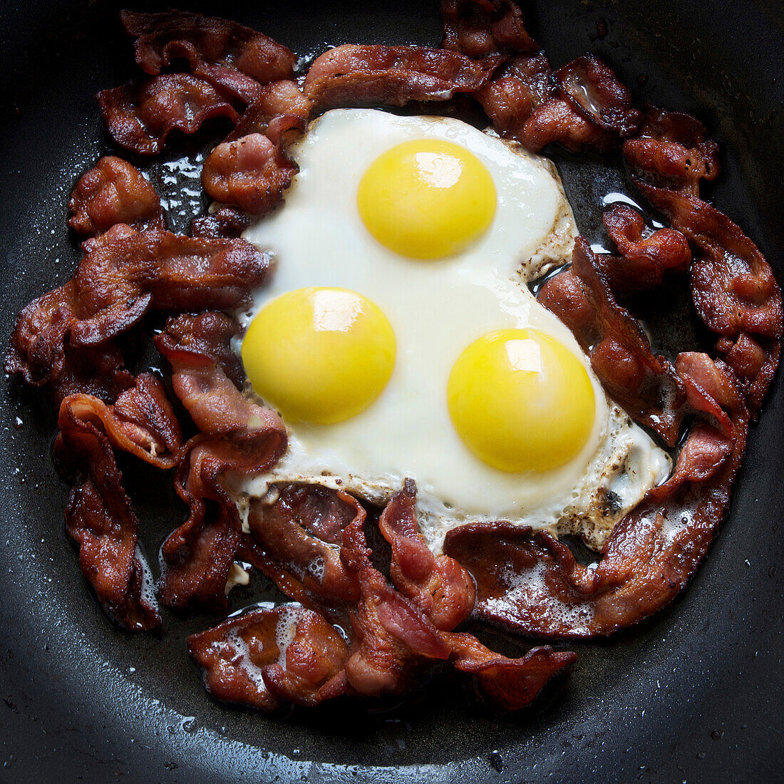 greasy frying pan full of bacon and eggs