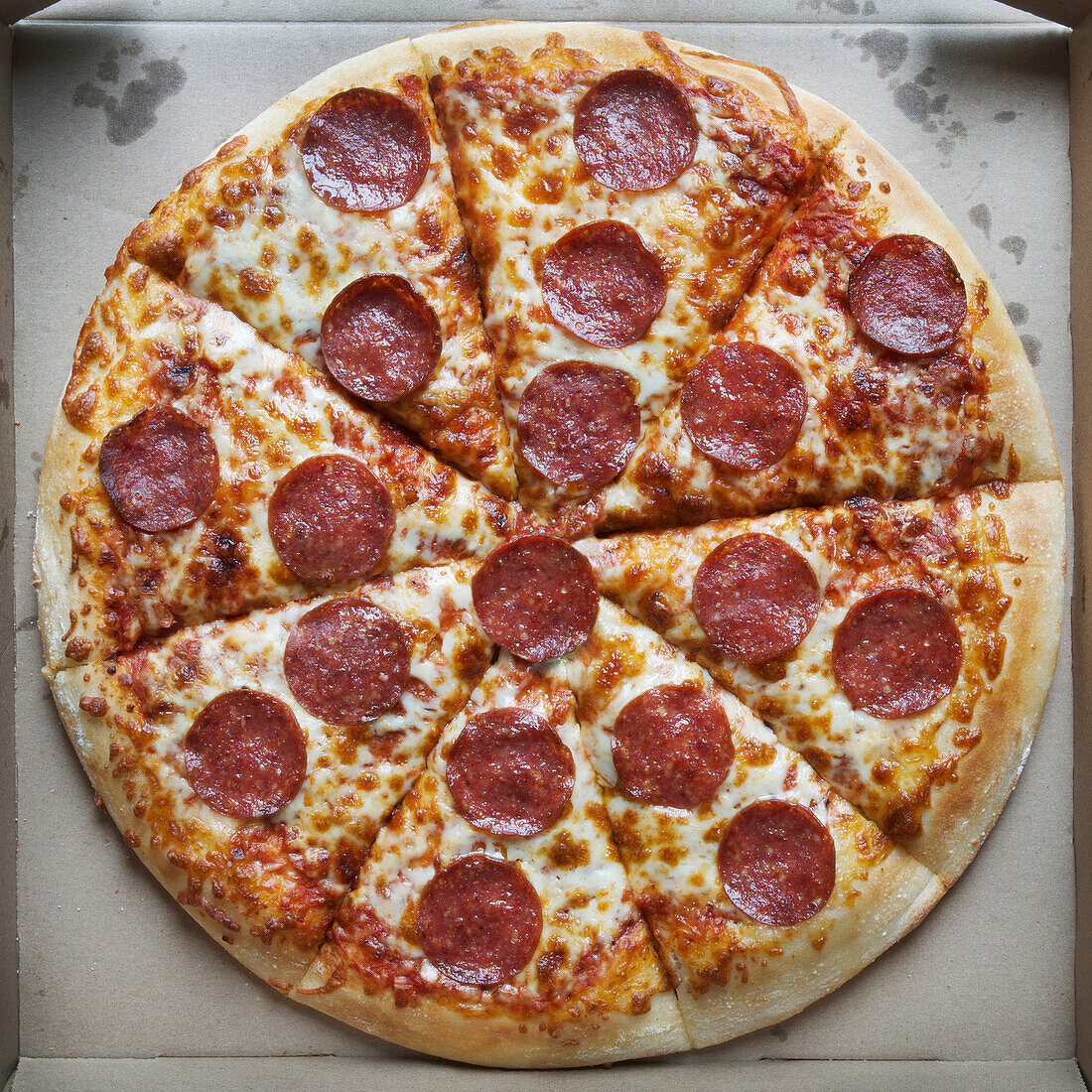 Draufsicht auf eine ganze Pizza mit Peperoni und Käse in einer Pappschachtel
