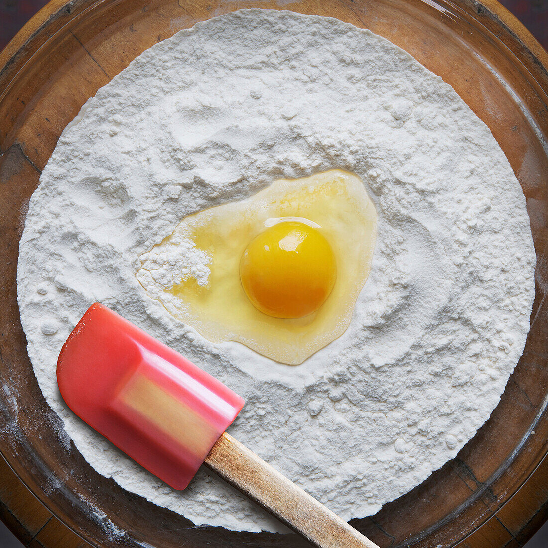 Nahaufnahme von Mehl und rohem Ei auf Glasschale mit Spachtel, Studioaufnahme