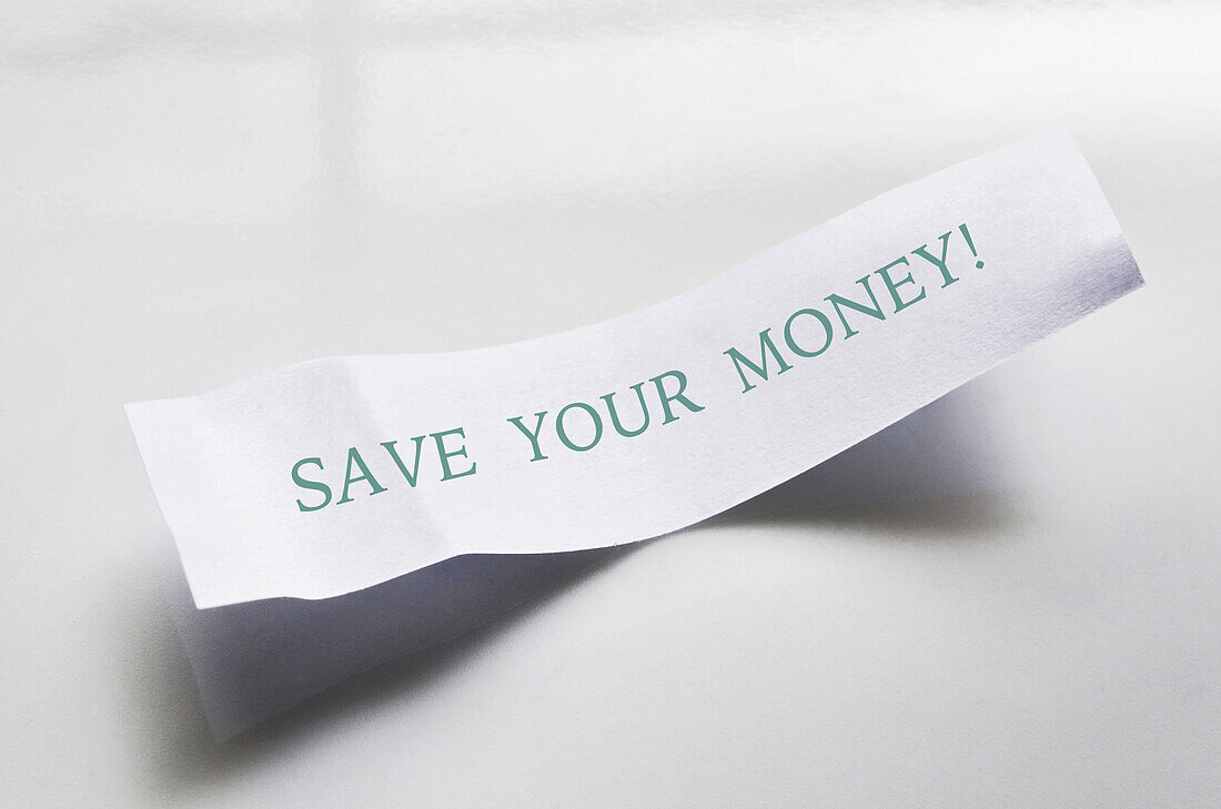 Close-up of message from fortune cookie on white plate, showing text for saving money, studio shot on white background