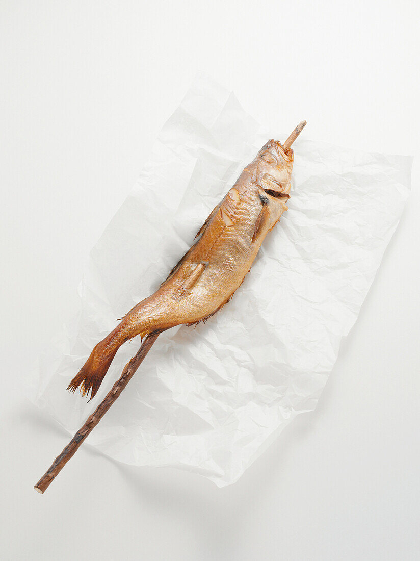 Fried mackerel pike fish on stick, on paper wrapper, studio shot