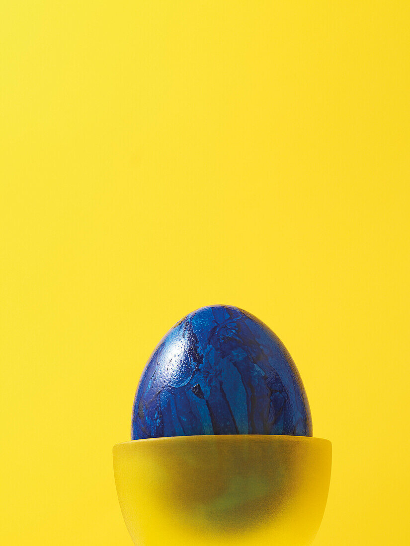 Blaues Osterei in gelbem Eierbecher