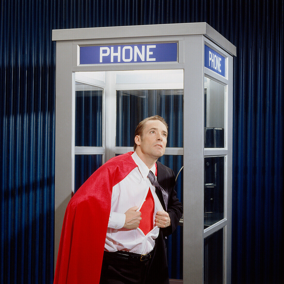 Mann öffnet Hemd, um Superheldenkostüm in Telefonzelle zu enthüllen