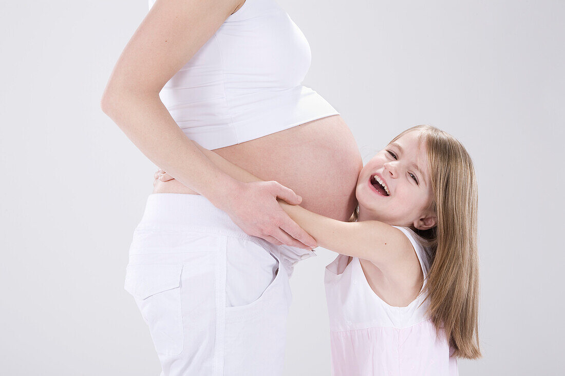 Kleines Mädchen umarmt schwangere Mutter