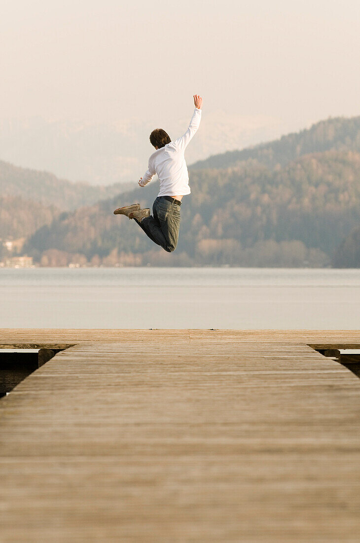 Mann auf Steg springt hoch in die Luft, Fuschlsee, Salzburger Land, Österreich