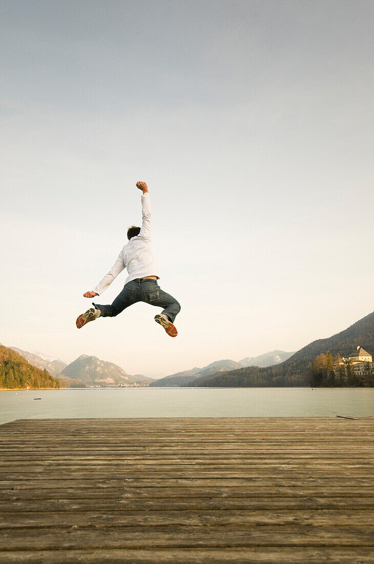 Mann auf Steg, der hoch in die Luft springt, Fuschlsee, Salzburger Land, Österreich