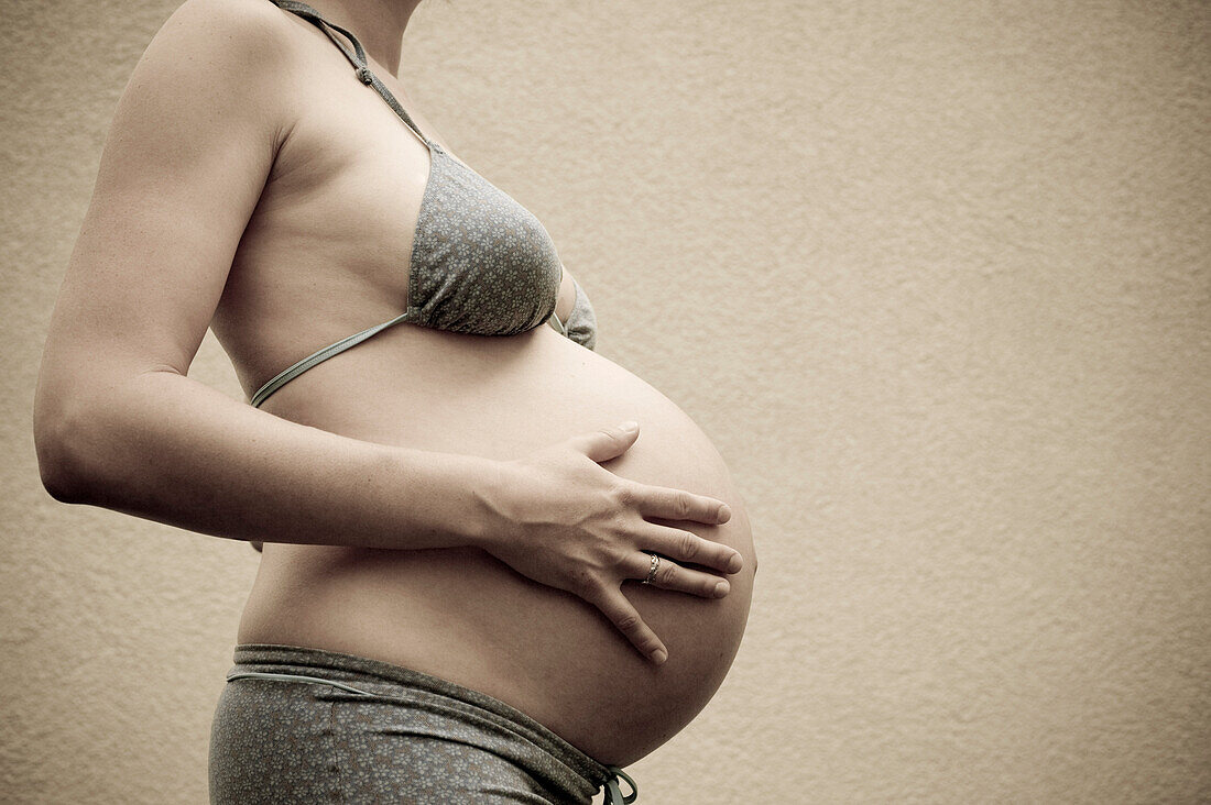 Profil einer im neunten Monat schwangeren Frau, die ihren Bauch berührt