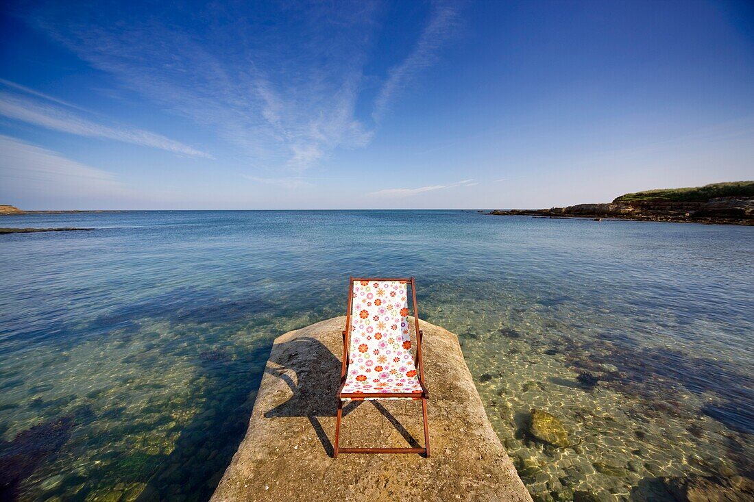 Northumberland, England; Empty Lawn Chair On Stone Wharf