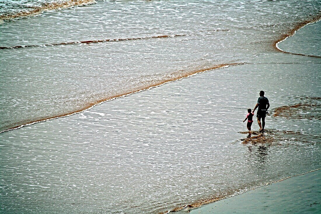 Vater und Sohn spazieren am Strand, Mann hält Angelrute; Sidmouth, Devon, England