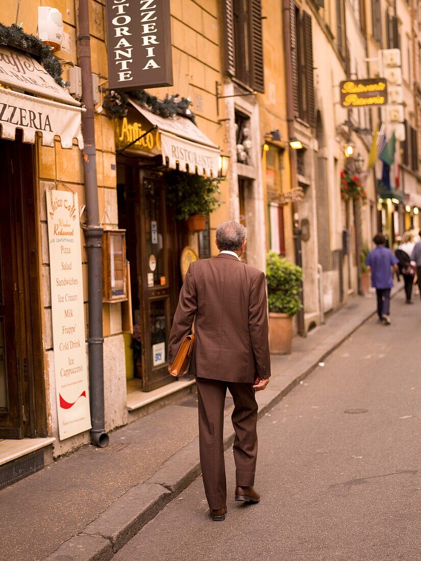 Rückansicht eines älteren Mannes, der auf der Straße geht und eine Aktentasche trägt; Rom, Italien